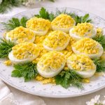 Creamy eggs mimosa (French deviled eggs) topped with finely grated egg yolk and fresh parsley on a white plate.