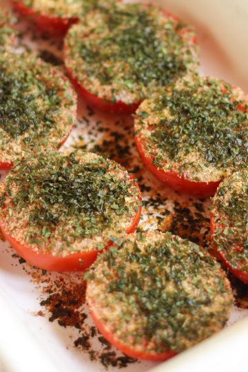 Baked Provençal tomatoes in a white dish, topped with garlic, herbs, and olive oil, slightly roasted and juicy.