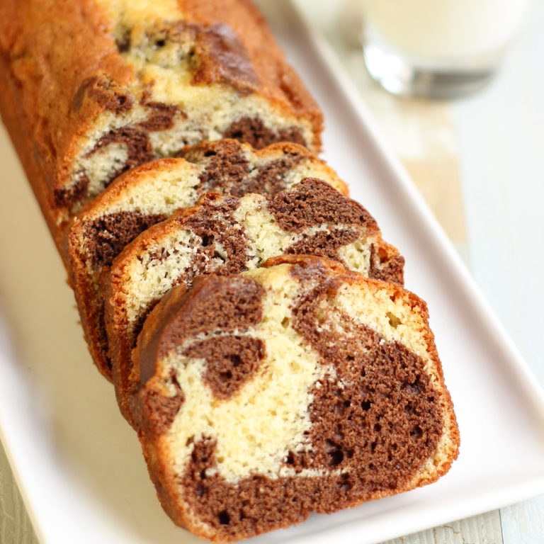 Sliced vanilla chocolate marble cake on a white platter with a glass of milk and eggs in the background