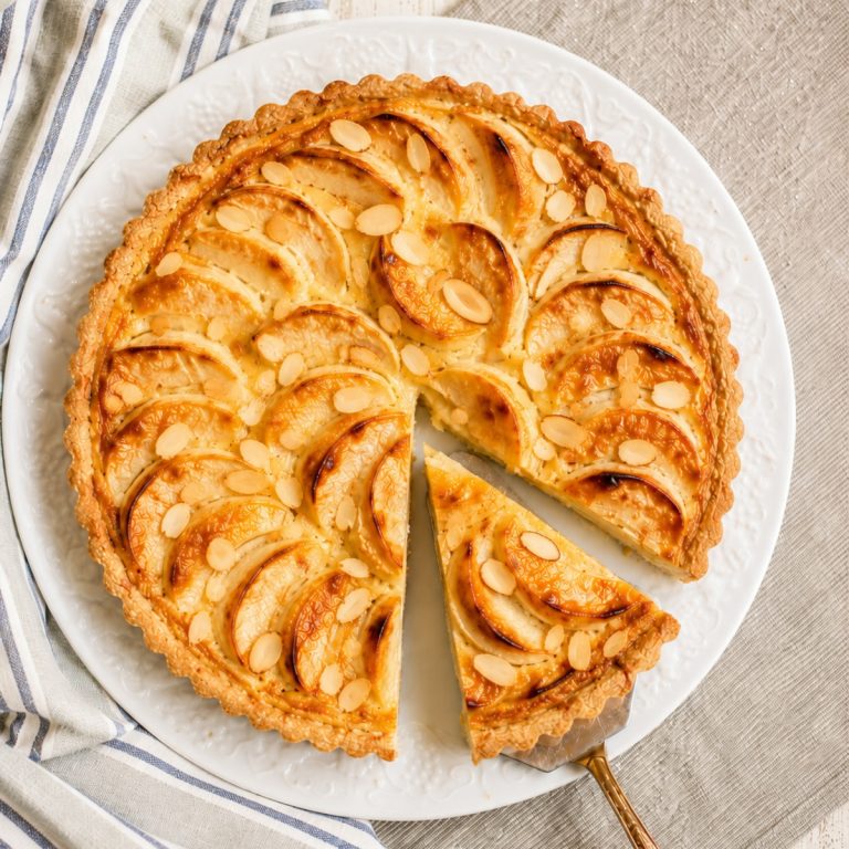 Whole Tarte Normande with sliced apples and almonds on a white tart plate
