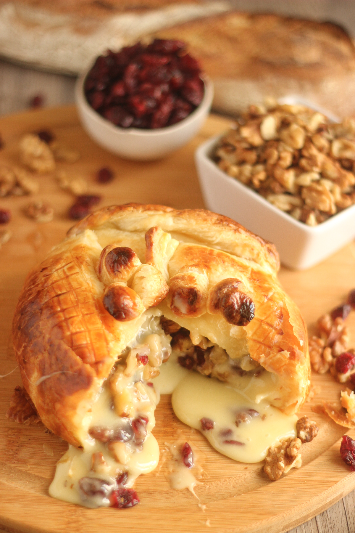 Baked Camembert with cranberries and walnuts wrapped in golden puff pastry, cut open to reveal warm melted cheese.