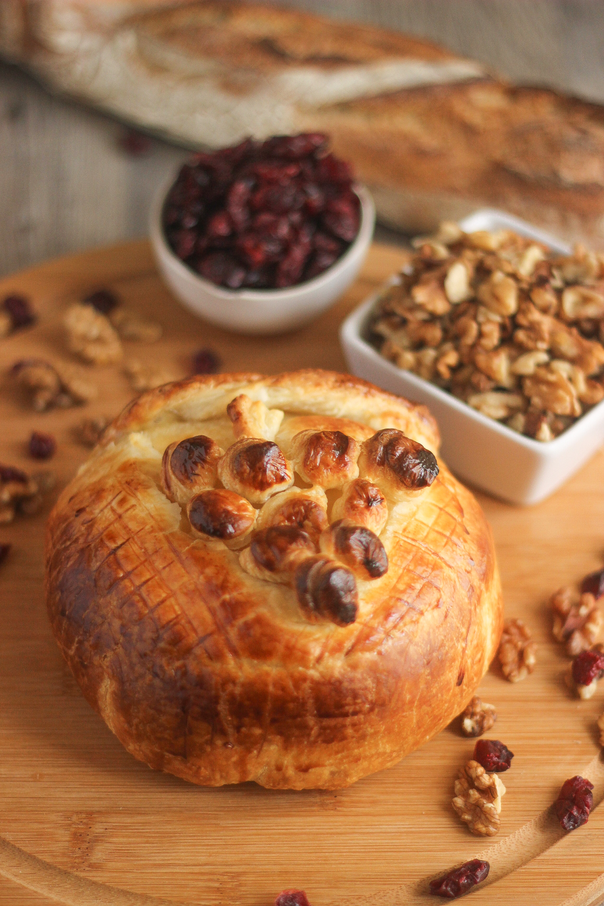 Whole baked Camembert:
Golden baked Camembert in puff pastry decorated with pastry grapes, with walnuts, cranberries and baguette in the background.