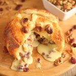 Baked Camembert with cranberries and walnuts wrapped in golden puff pastry, cut open to reveal warm melted cheese.