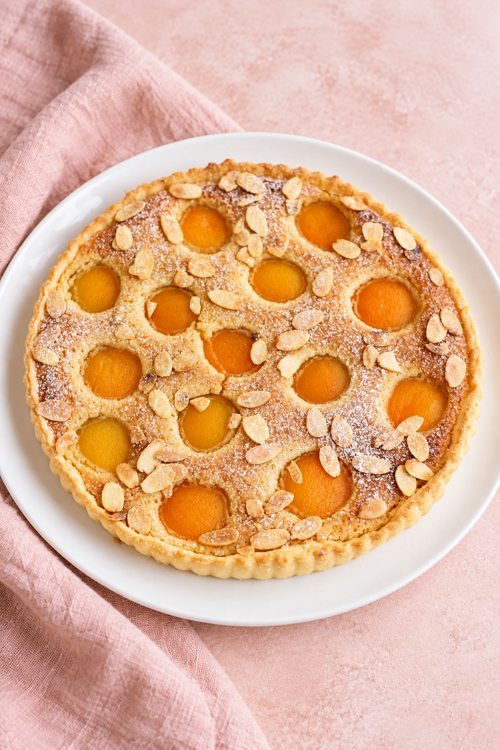 Baked apricot frangipane tart decorated with sliced almonds and a light dusting of powdered sugar.