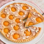 Easy French apricot frangipane tart with almond cream, sliced almonds, and powdered sugar.