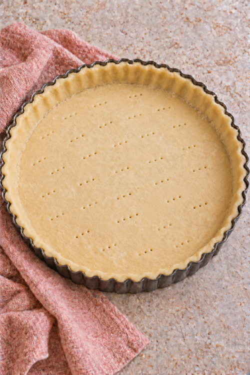 Unbaked pastry crust fitted inside a round fluted tart pan.